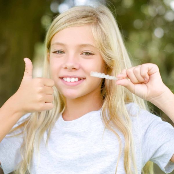 MODEL holding an invisible braces aligner and rising thumb up, recommending this new treatment. Dental healthcare concept.
