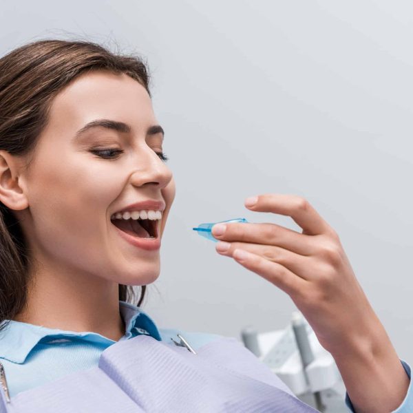 cheerful woman with opened mouth holding retainer in dental clinic